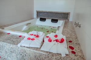 塞古罗港Orquídeas Praia Hotel的浴缸配有2条白色毛巾和红色玫瑰