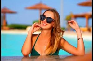 赫尔格达Juliana Beach Hurghada的坐在游泳池旁桌子旁的戴太阳镜的女人