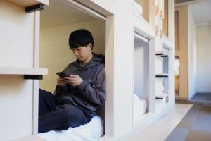 东京Hotel Tomariya Ueno的坐在窗户旁看手机的男孩