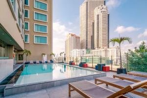 曼谷Hilton Garden Inn Bangkok Silom的一座带长椅和高楼建筑的游泳池
