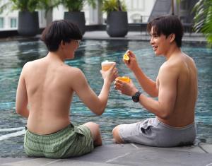 曼谷Aira Hotel Bangkok Sukhumvit 11的两个坐在泳池旁吃食物的年轻人