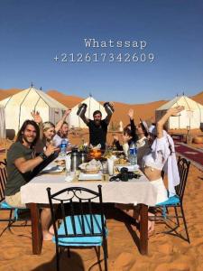 梅尔祖卡Blue Sky Luxury Camp的一群人坐在沙漠的桌子旁