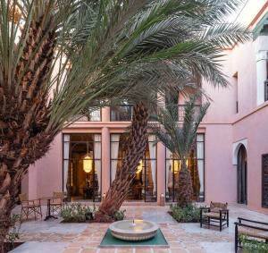 马拉喀什Riad Dar Al Dall - This Time Tomorrow in Marrakech的一座粉红色建筑前方种有棕榈树的庭院