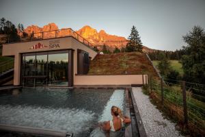 新黎凡特Moseralm Dolomiti Spa Resort的坐在游泳池的女人,坐在房子前