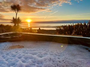 霍基蒂卡Drifting Sands Beachfront Retreat的享有日落美景的热水浴池