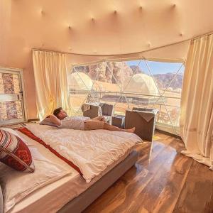 瓦迪拉姆desert wadi rum camp的一个人躺在带大窗户的房间的床上