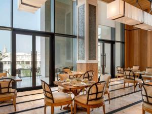多哈Alwadi Hotel Doha - MGallery的餐厅设有桌椅和大窗户。