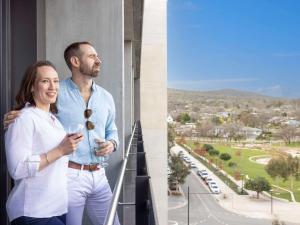 堪培拉The Sebel Canberra Campbell的男人和女人站在阳台上喝一杯葡萄酒