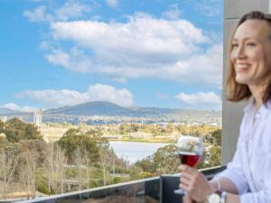 堪培拉The Sebel Canberra Campbell的一位女士在阳台上喝一杯葡萄酒