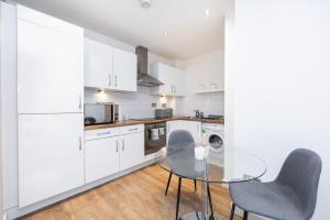 伦敦Modern 1 BR Apartment Near Shoreditch - 10 Min Walk的厨房配有白色橱柜和玻璃桌椅