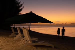 Susupe塞班岛世界度假酒店的两个人站在海滩上,在伞下