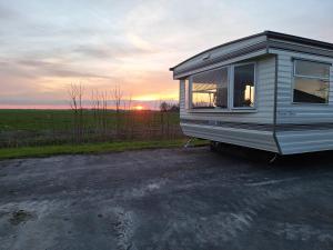BurumStacaravan Elly, Minicamping de Grutte Earen的停泊在停车场的拖车,背面是日落