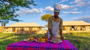 塞伦盖蒂国家公园Serengeti Malaika Luxury Camp的一个人站在餐桌旁吃着食物