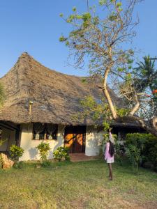 MsambweniSansuri Beach House的站在茅草屋顶房子前面的女人