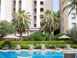 达喀尔诺富特达喀尔酒店的一个带椅子和遮阳伞的游泳池以及棕榈树