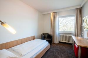 莱茵河畔威尔Ott's Hotel Weinwirtschaft & Biergarten Weil am Rhein/Basel的一间卧室配有一张床、一张书桌和一个窗户。