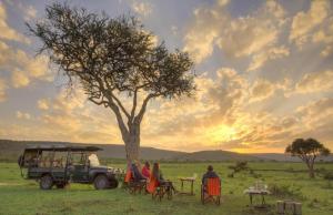 Sekenanisunshine maasai Mara safari camp in Kenya的一群坐在树下桌子上的人
