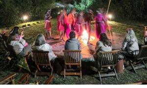 Sekenanisunshine maasai Mara safari camp in Kenya的一群人坐在椅子上,围着火炉