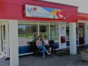 曲马勒姆Chalet with garden near Wadden Sea的两个女人坐在商店外的长凳上