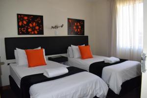 约翰内斯堡Premiere Classe Apartment Hotel的客房配有两张带橙色和白色枕头的床。