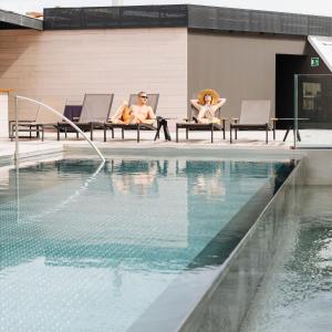巴塞罗那奥利维亚巴美思酒店的两人坐在游泳池旁的椅子上