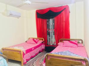 伊斯梅利亚Chalets and apartments Al-Nawras Village Ismailia的配有红色窗帘的客房内的两张床