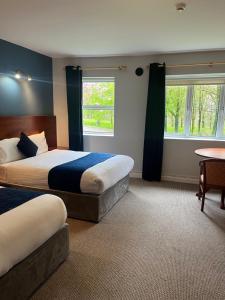 科克Fernhill Lodge Carrigaline的一间卧室设有两张床、一张桌子和两个窗户。