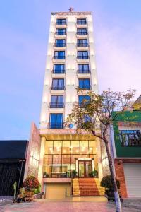 岘港Nostalgia Boutique Hotel的一座高大的白色建筑,前面有一棵树