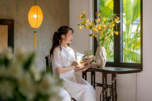 会安Nghé Garden Resort Hội An by Label6的坐在桌子上的穿着白色衣服的女人,带蛋糕