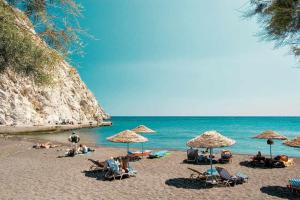 佩里萨Santorini Seaside Retreat - Flora's Summer Escape的一群人坐在海滩上,拿着遮阳伞