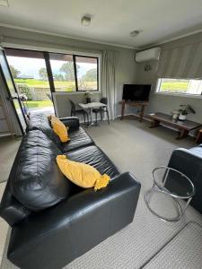 芒格努伊山Coastal Golf & Spa Guesthouse的客厅配有带黄色枕头的黑色皮沙发