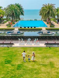 汕尾汕尾保利希尔顿逸林酒店的家庭在游泳池前的草地上散步