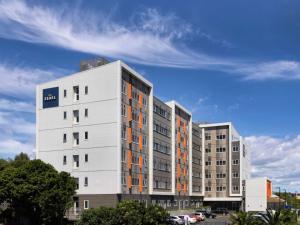 奥克兰The Sebel Auckland Manukau的白色的公寓大楼,拥有橙色的窗户和蓝色的天空