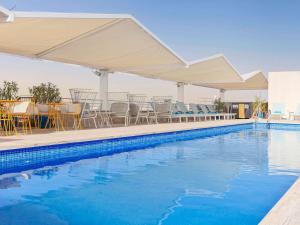 塞维利亚Novotel Sevilla的一个带桌椅和遮阳伞的游泳池