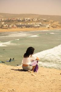 塔姆拉赫特乌兹达尔Darna Surf House Morocco的坐在海滩上看着大海的女人