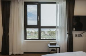 西归浦市Lemain Hotel Seogwipo的卧室设有大窗户和白色窗帘