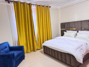 NamugongoKamona Living的一间卧室配有黄色窗帘、一张床和一张蓝色椅子