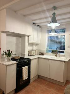 阿什伯恩Rosie Cottage的厨房配有白色橱柜和黑炉灶烤箱。