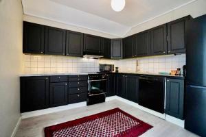 波什格伦Sentralt i rolig bygård, med heis, egen, veranda & 85" Smart TV的厨房配有黑色橱柜和红色地毯
