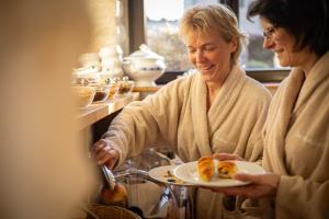 斯滕奥克尔泽尔毕佛特温泉酒店的两个年纪较大的妇女一起坐在一起,拿着一盘食物