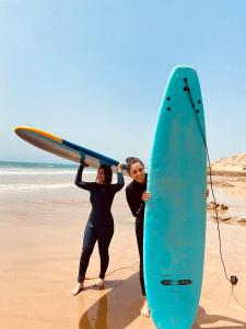 Tamraght Ou FellaSurfpoint Tamraght的两名妇女站在海滩上,并带有冲浪板