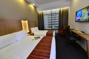 新加坡Hotel Grand Central的酒店客房设有两张床、一张桌子和一台电视。