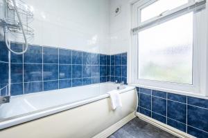 纽波特Dos Road by Tŷ SA的蓝色瓷砖浴室设有浴缸和窗户。