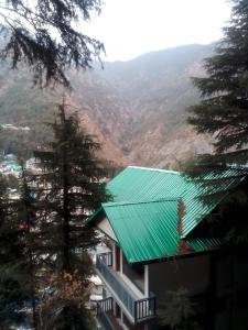 达兰萨拉Himalayan Mountain View的一座带绿色屋顶的建筑,背景是群山