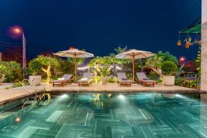 会安Villa Dương Hội An的夜间游泳池,配有椅子和遮阳伞