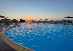 阿莱曼Blumar Sidi Abdel Rahman 2 bedrooms Chalet North Coast的一座蓝色的大型游泳池,背面是日落