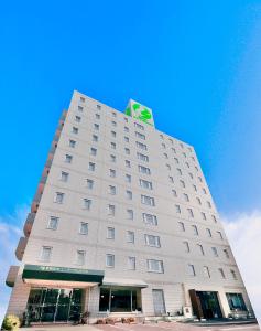 仓敷Kurashiki Ekimae Universal Hotel的上面有绿色标志的高大的白色建筑