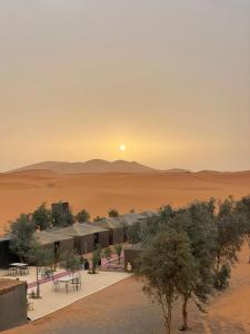 梅尔祖卡Mustapha Camp Merzouga的沙漠中的一座建筑,背景是日落