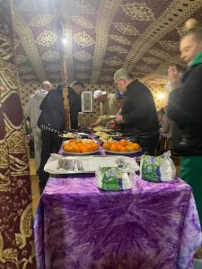 梅尔祖卡Mustapha Camp Merzouga的一群人站在桌子旁,一边吃橙子