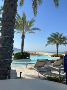 马斯喀特Water Front Villa BF108的海滩上带椅子和棕榈树的游泳池